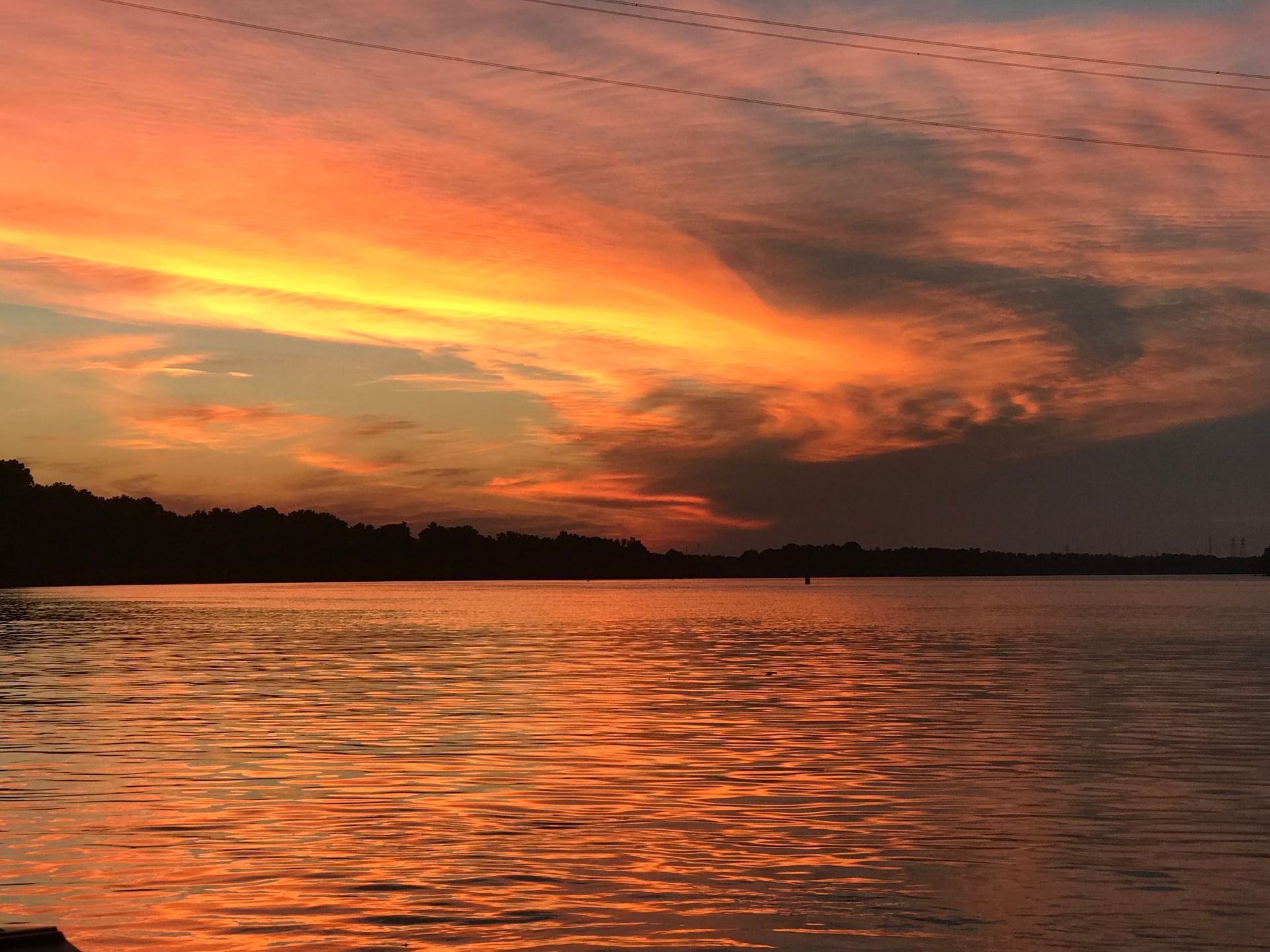 Fiery orange sunset over a calm lake with dark shoreline silhouettes and rippled water reflections