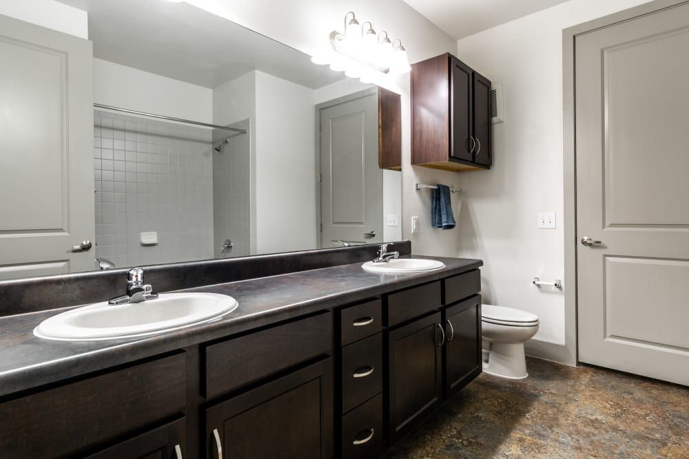 Student apartment bathroom with two sinks, a toile, and a large mirror at Regents West at 26th in Austin, TX, near UT Austin.