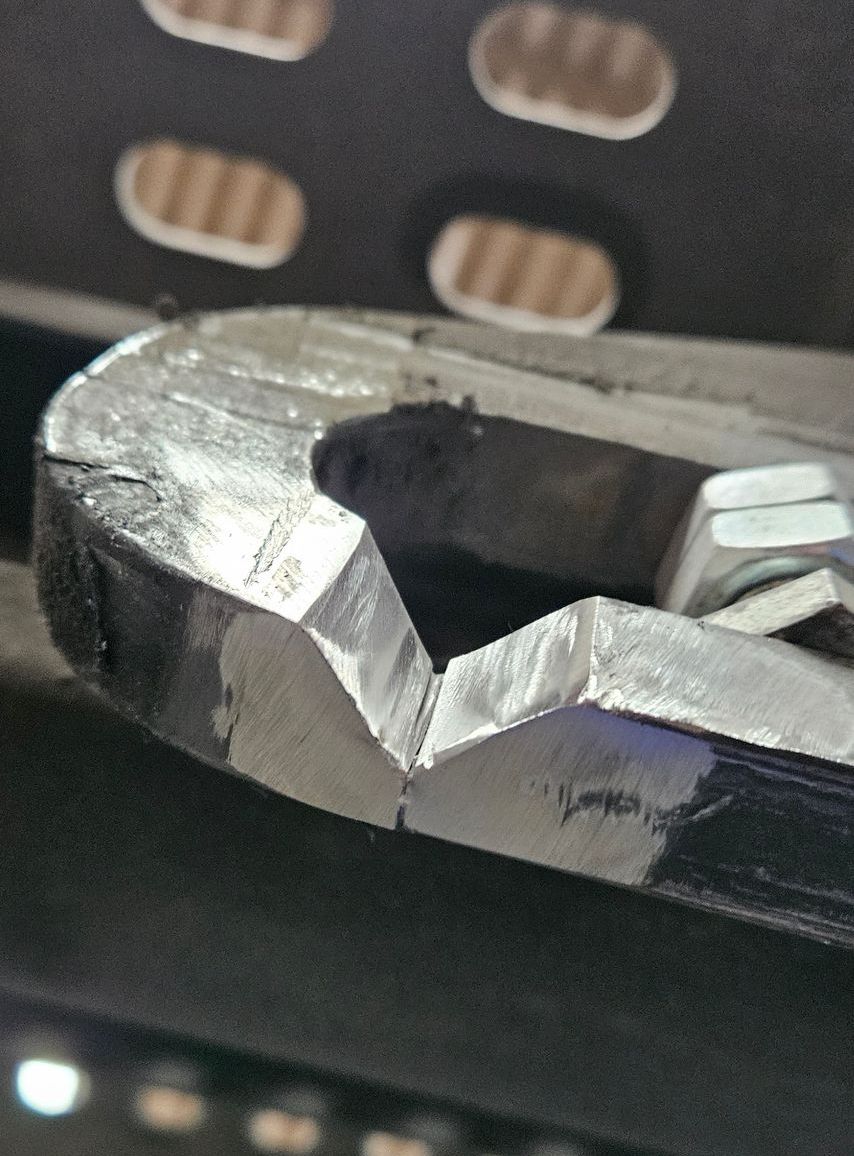 Close-up of a silver metal wrench gripping a black hex nut against a dark, perforated background