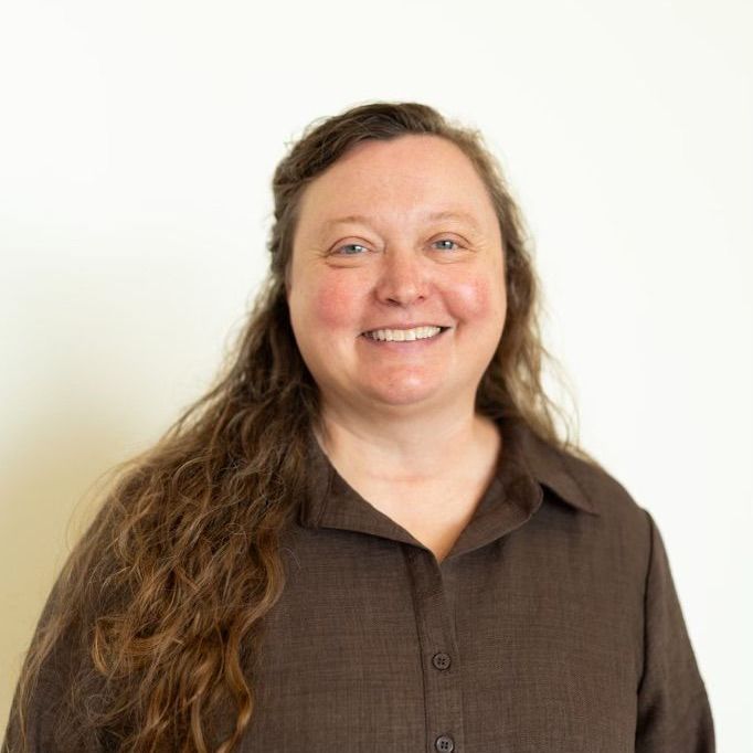 Woman with long brown hair smiles, wearing a brown collared shirt against a white backdrop.