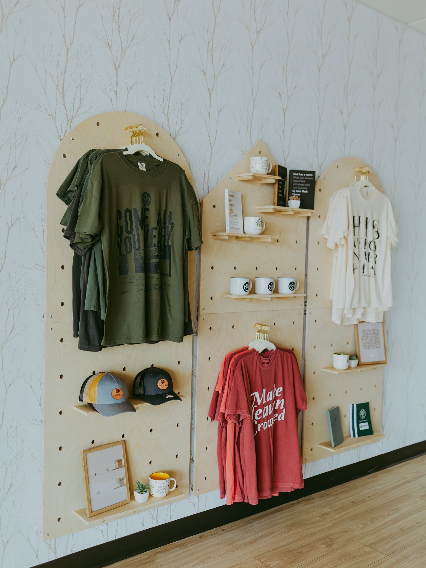 Merchandise display with t-shirts, hats, and mugs on wooden shelves against a textured wall.