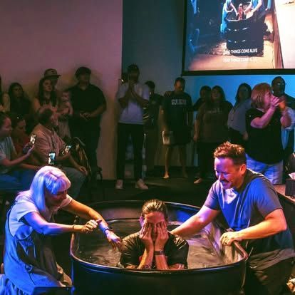 Two people assist a woman standing in a baptismal pool during a church ceremony