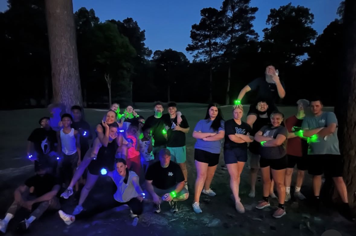 Group of people posing with glowing green and blue lights outdoors at night.