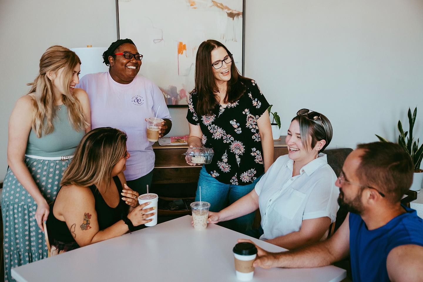 Six people chatting around a table with coffee cups in a bright room