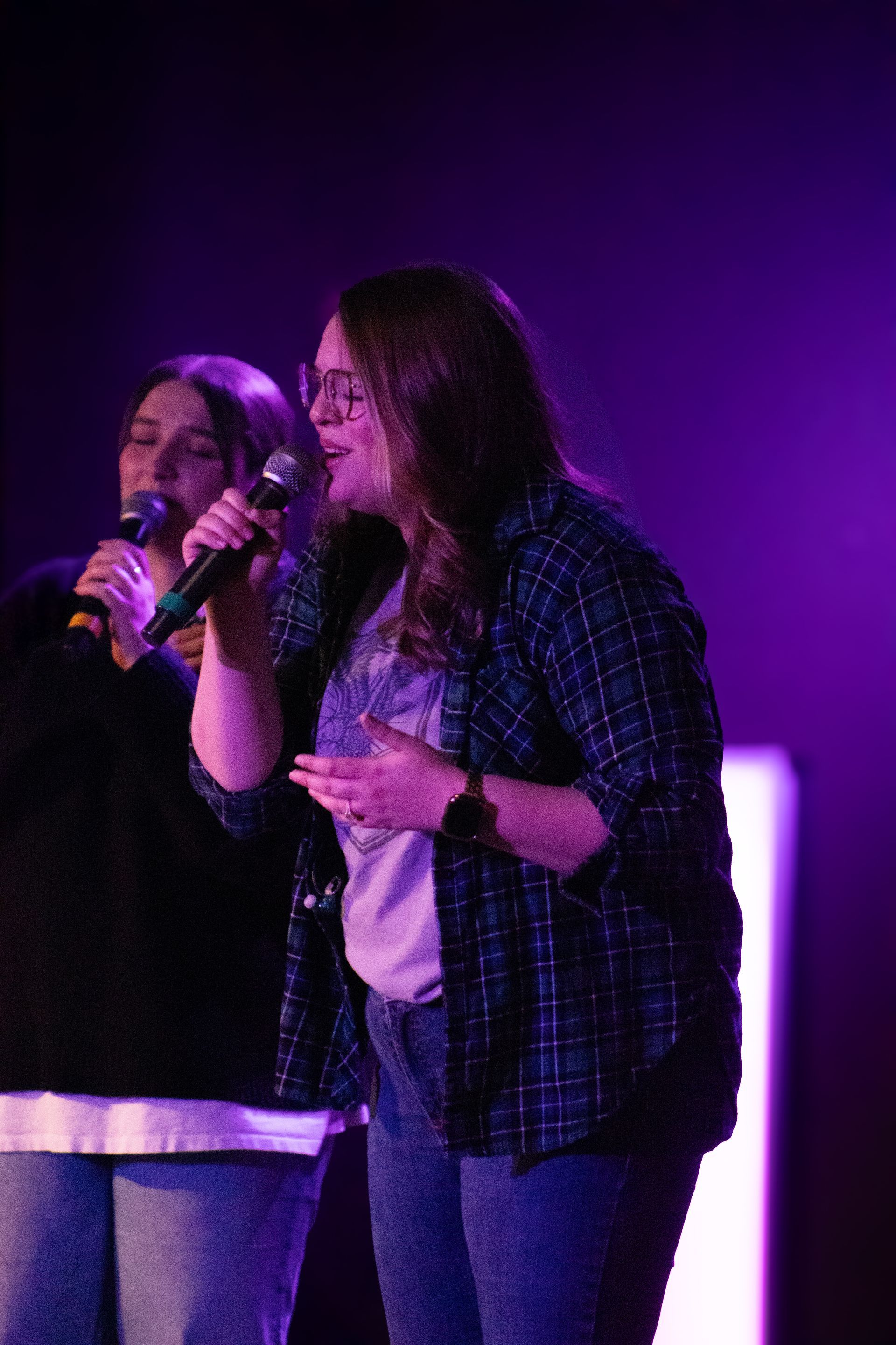 Two singers holding microphones on a purple-lit stage