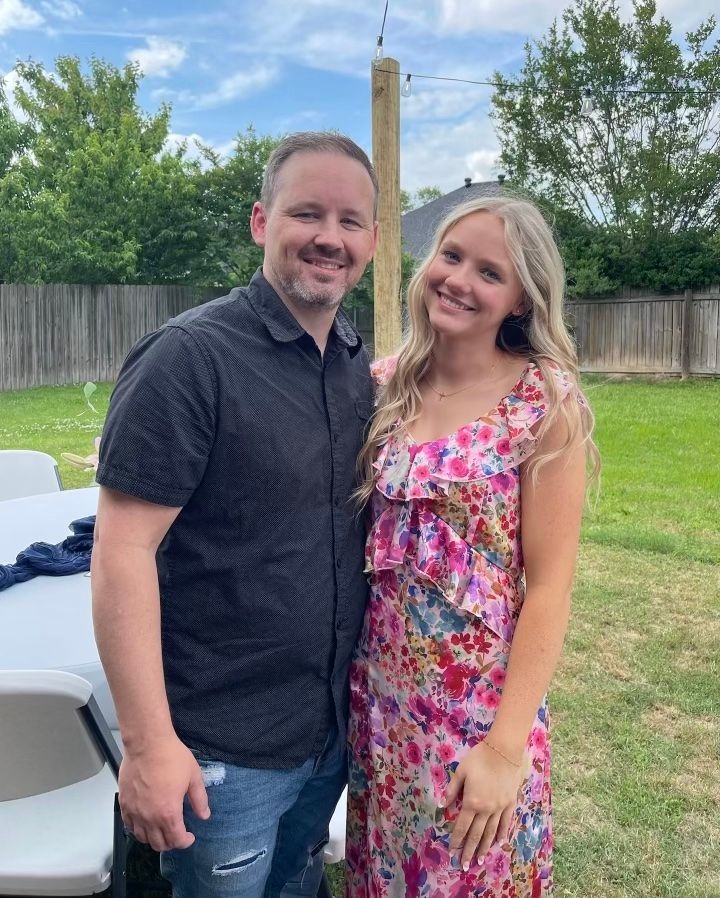 Man in black shirt and woman in floral dress smiling outdoors.