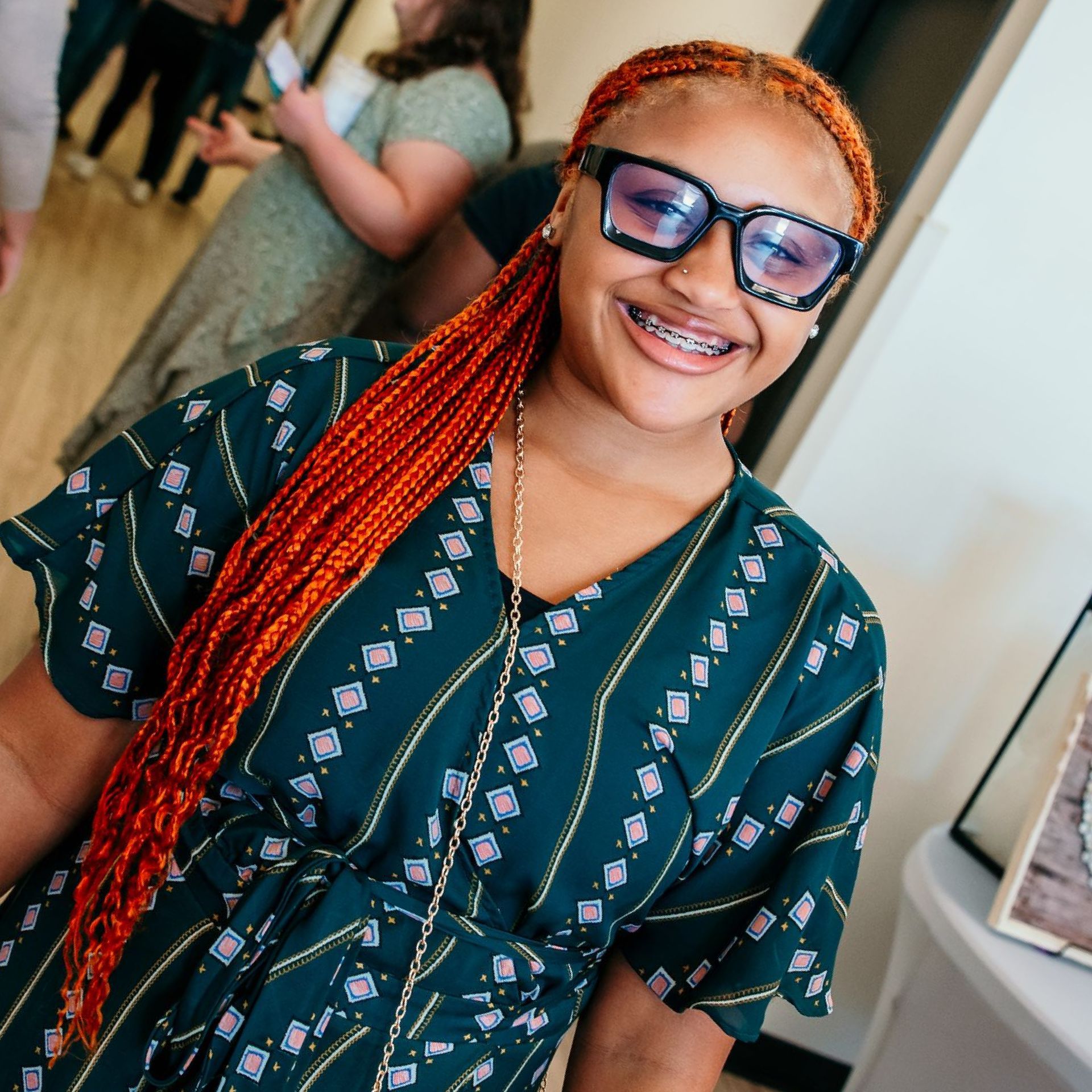 Woman with orange braids and glasses smiles in a green dress.
