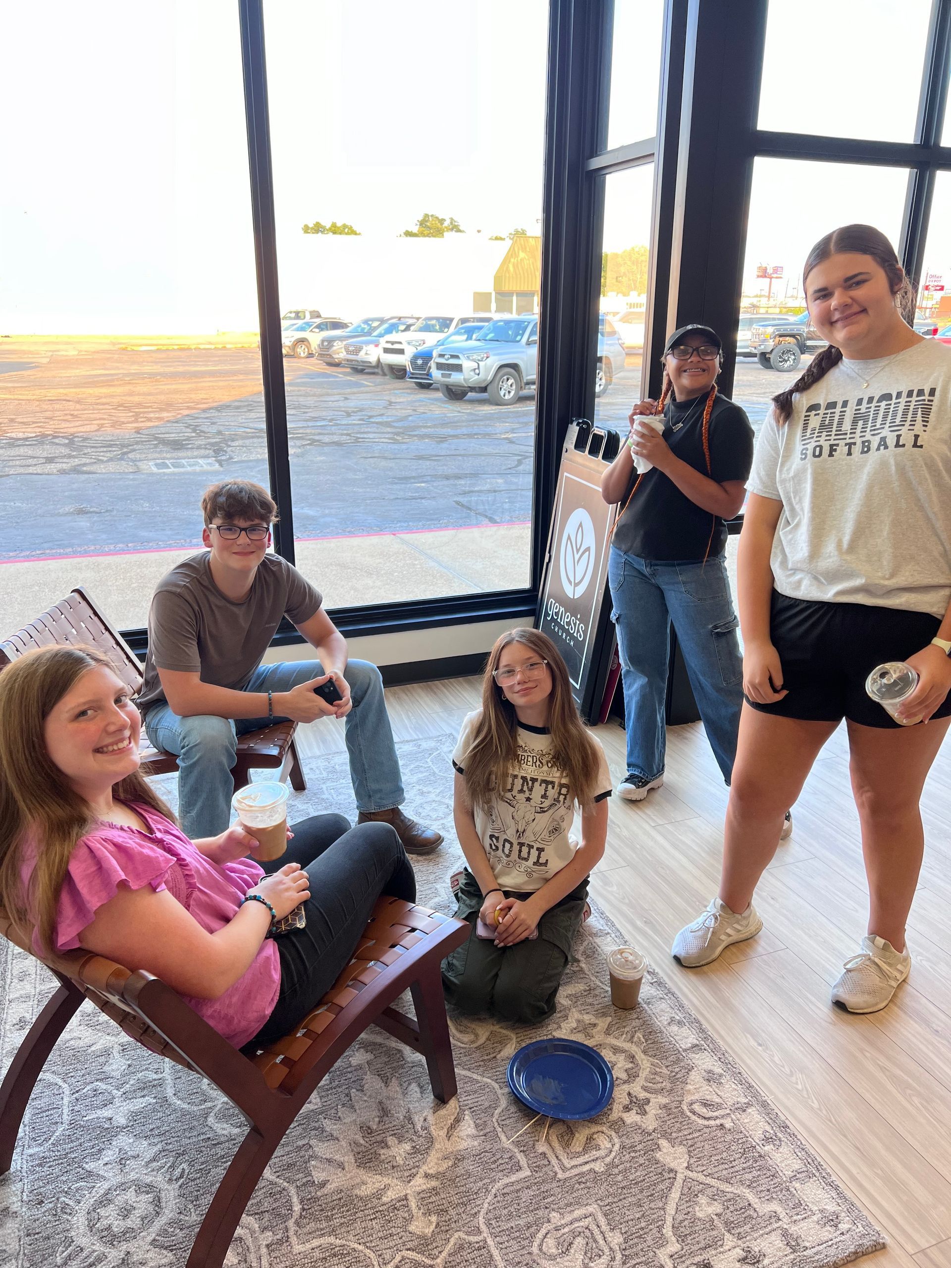 Group of people indoors by large window. Some seated, some standing, smiling.