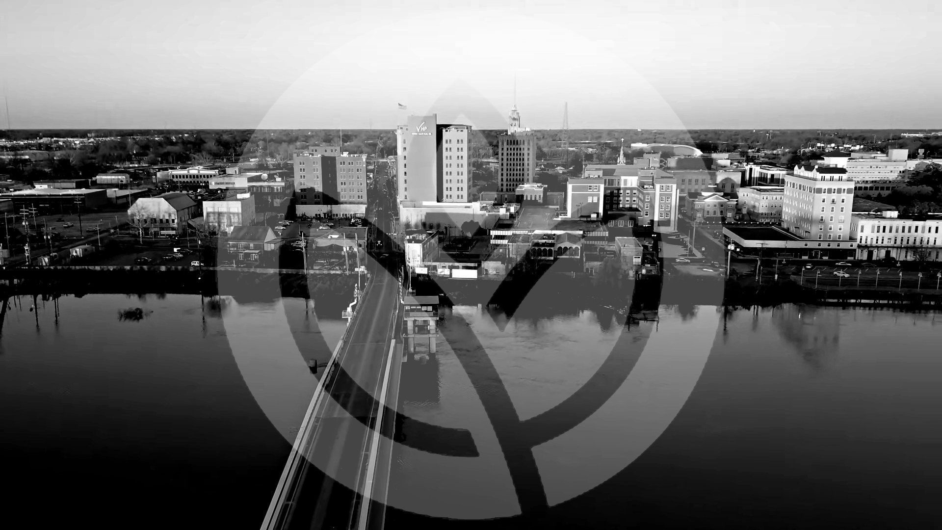 City skyline with bridge, obscured by a partially transparent circular logo over the image.