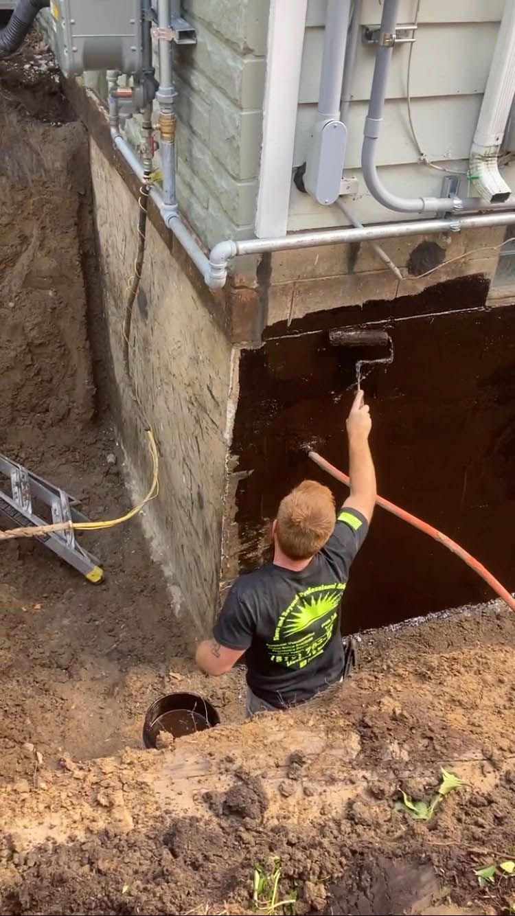 A man is painting a basement wall with a roller.