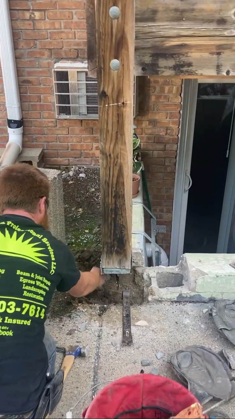 A man is working on a wooden post in front of a brick building.