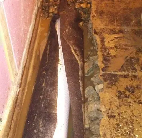 A white pipe is coming out of a hole in a wall.