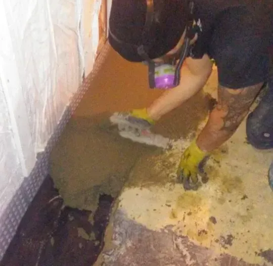 A man wearing a gas mask and gloves is working on a concrete floor.