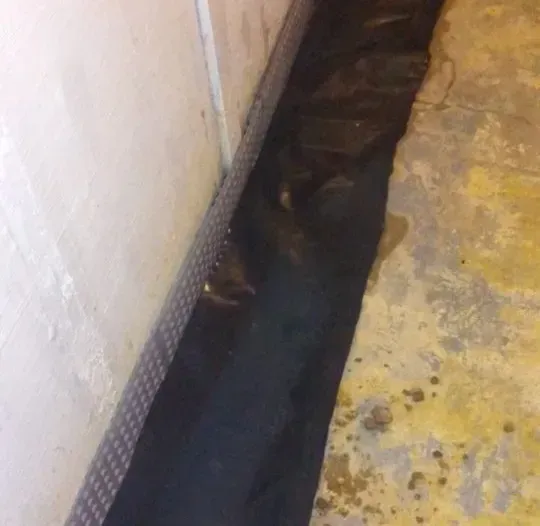 A black tarp is covering a concrete floor next to a wall.