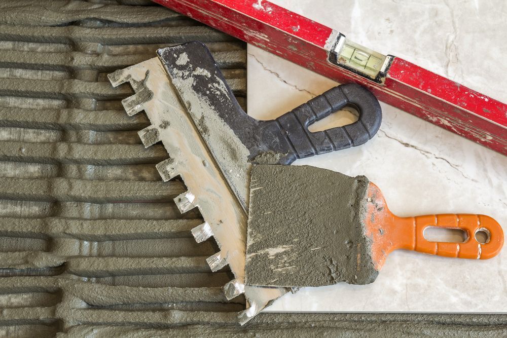A Adhesive Spreader, Trowel And A Level Are Laying On A Tile Floor — Twin Towns Sand & Gravel In Tweed Heads South, NSW
