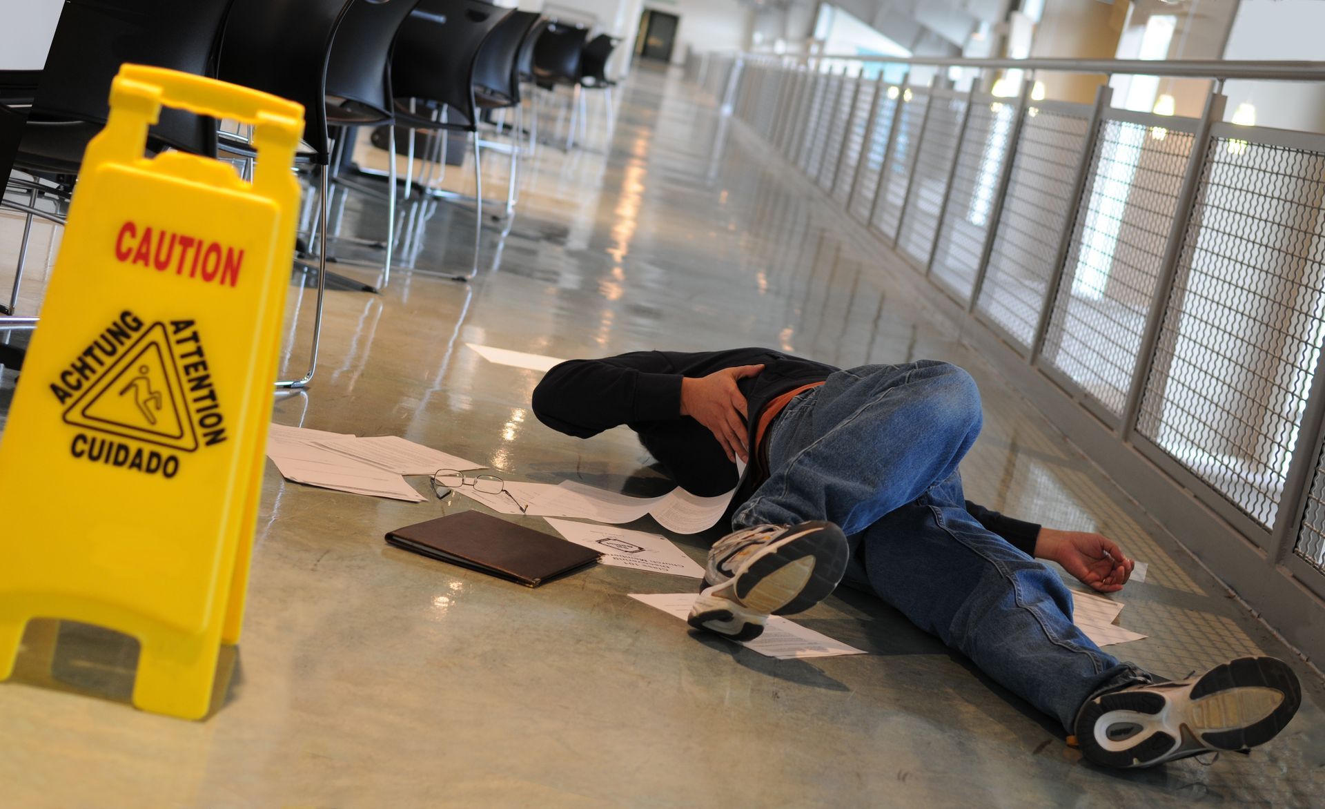 A person lying on a shiny floor next to scattered papers and a tablet.