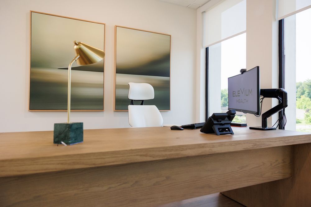 Minimalist office desk with dual monitors, white chair, and framed abstract art on the wall.