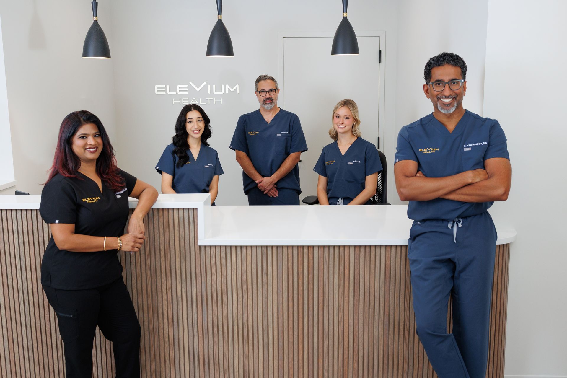 Five staff members stand behind a white reception desk in a modern clinic lobby.