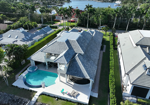 Aerial view of a luxurious waterfront home with a pool, palm trees, and canal in the background.
