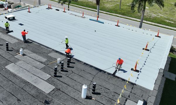 Roofers installing a new white membrane roof on a building. Safety cones, lines, and vents are present.