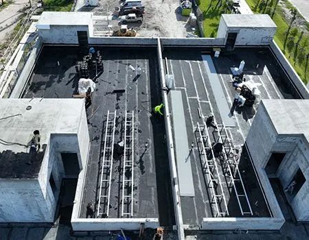 Aerial view of a flat roof construction site with workers, ladders, and building materials.