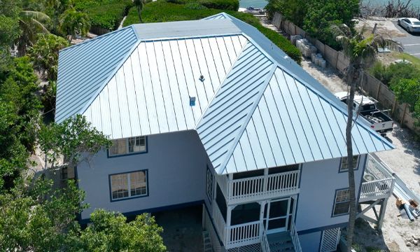 House with a light blue metal roof and siding, two stories, front porch, surrounded by greenery.