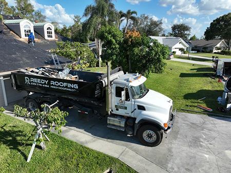 A white Reedy Roofing truck parked in a driveway with debris, roof work underway.