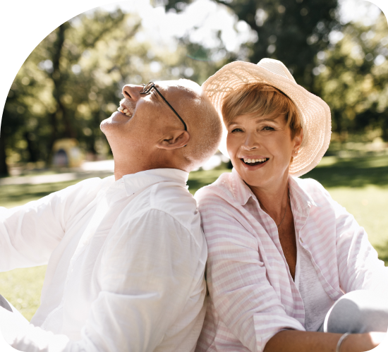 Two smiling people in hats sitting outdoors in a sunny park