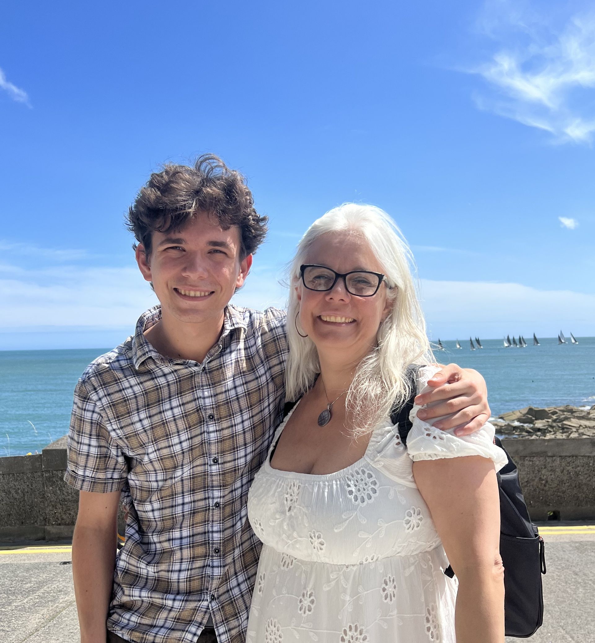 Two people smiling by the ocean under a bright blue sky