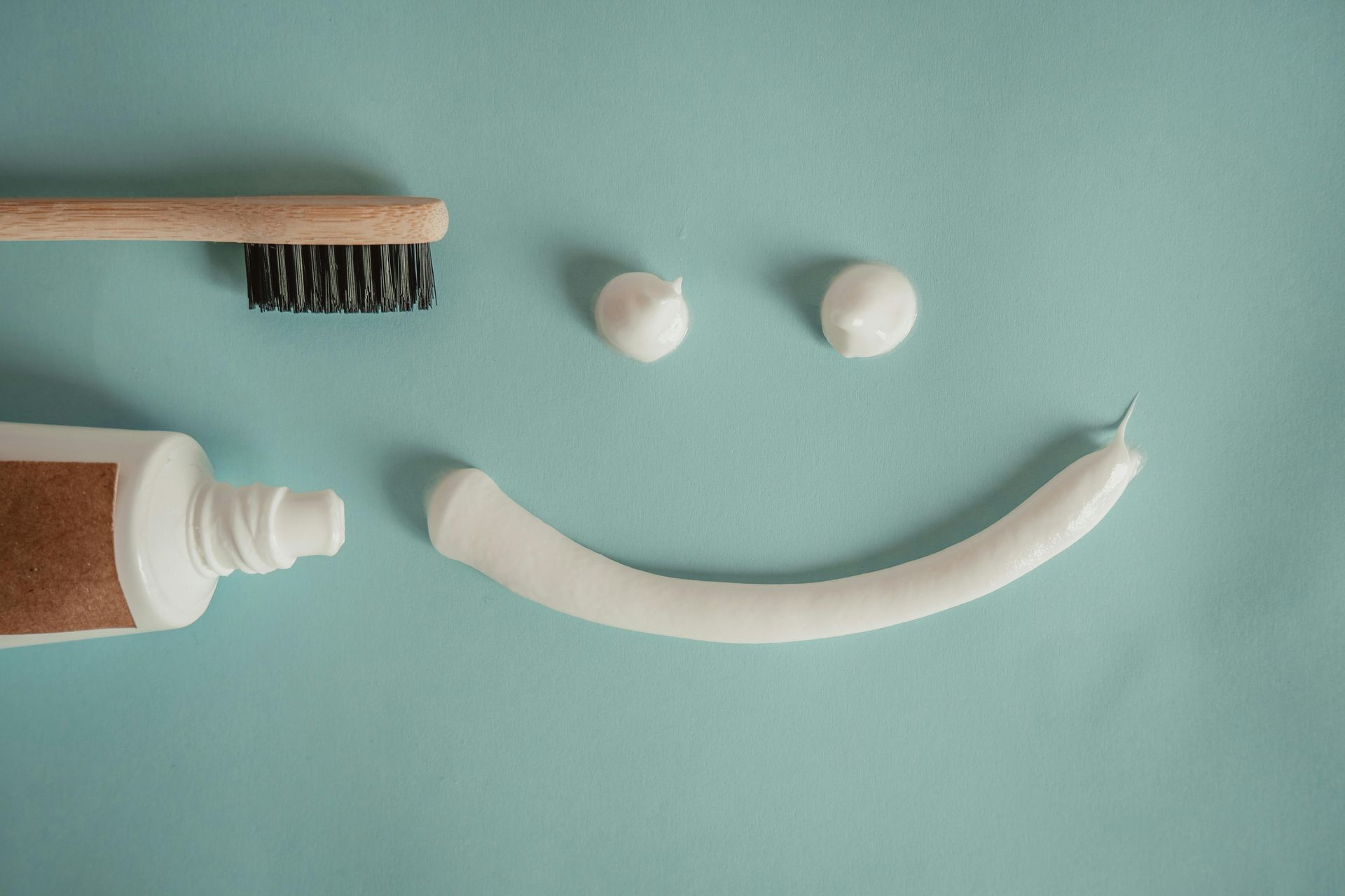 A toothbrush, toothpaste, and two dollops of toothpaste arranged on blue to form a smiling face.