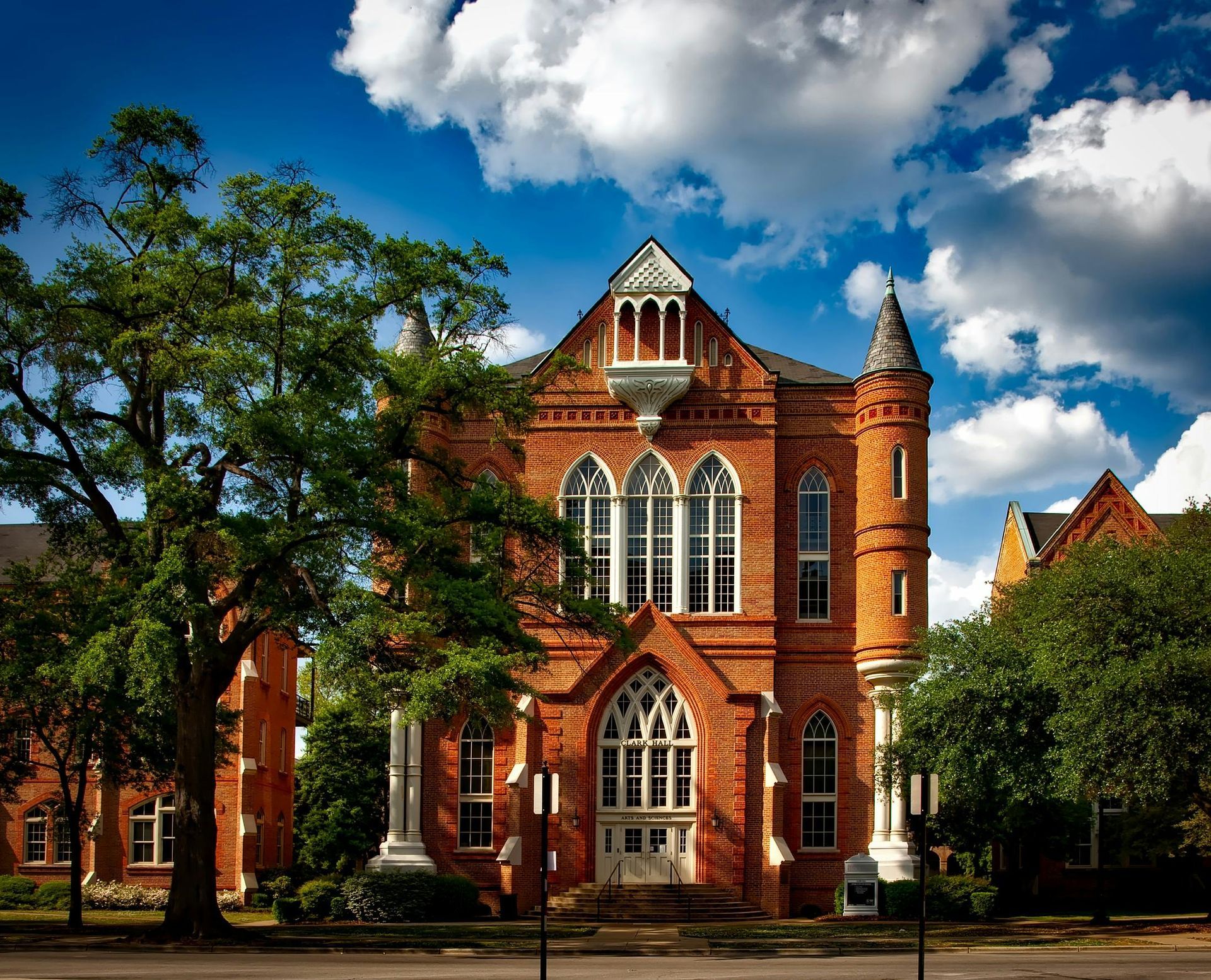 Brick building with arched windows, tower, and ornate details under a partly cloudy blue sky.