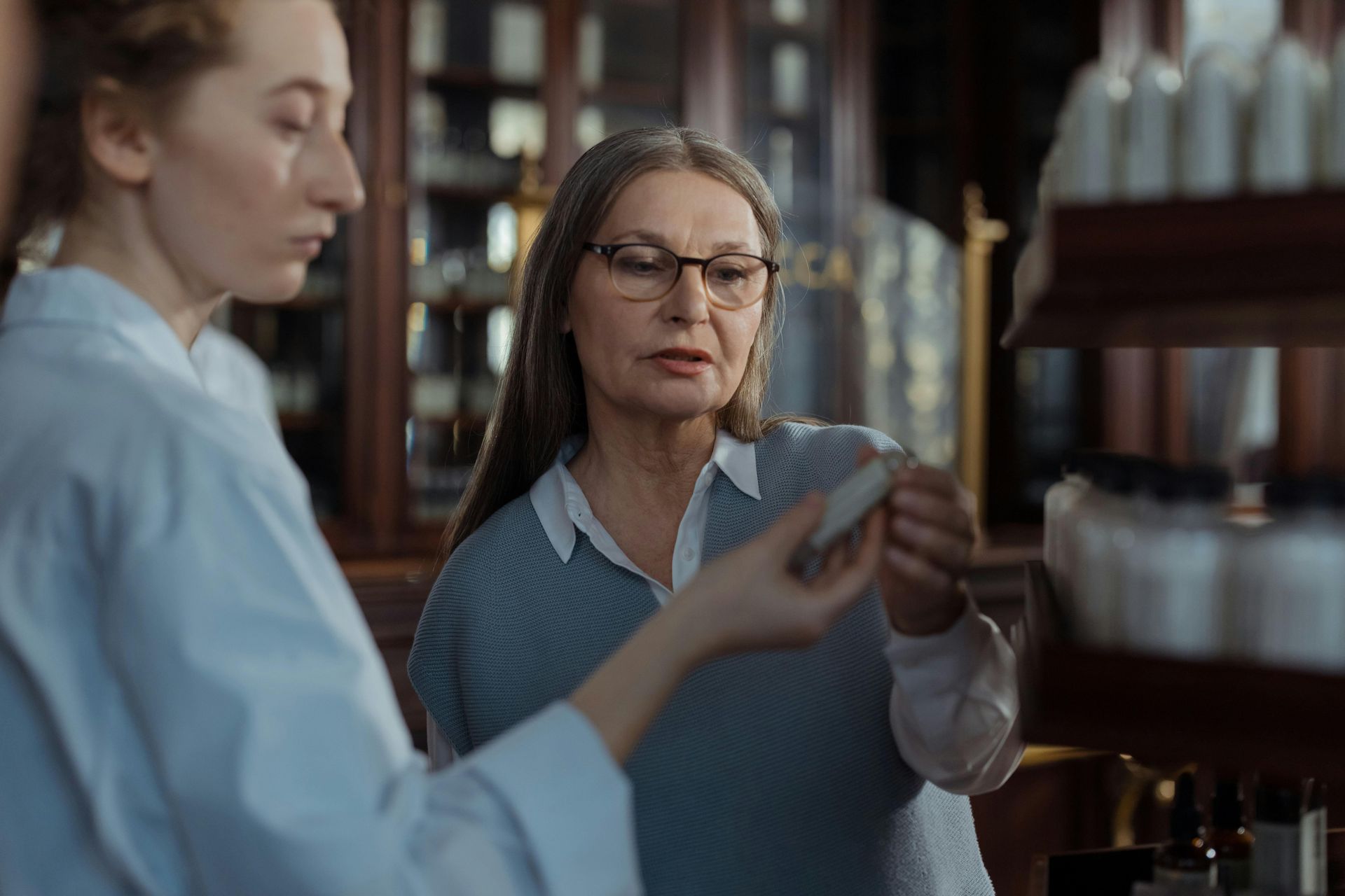 Woman in glasses examines a small object with a person in a lab coat in a laboratory setting.
