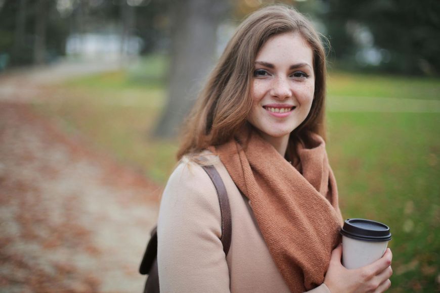 Younger woman smiles outside with coffee near a trail in Carmel, Indiana
