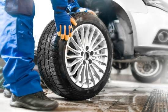 A Man is Holding a Tire in Front of a Car — High Grade Tyre and Mechanical in Toowoomba City, QLD