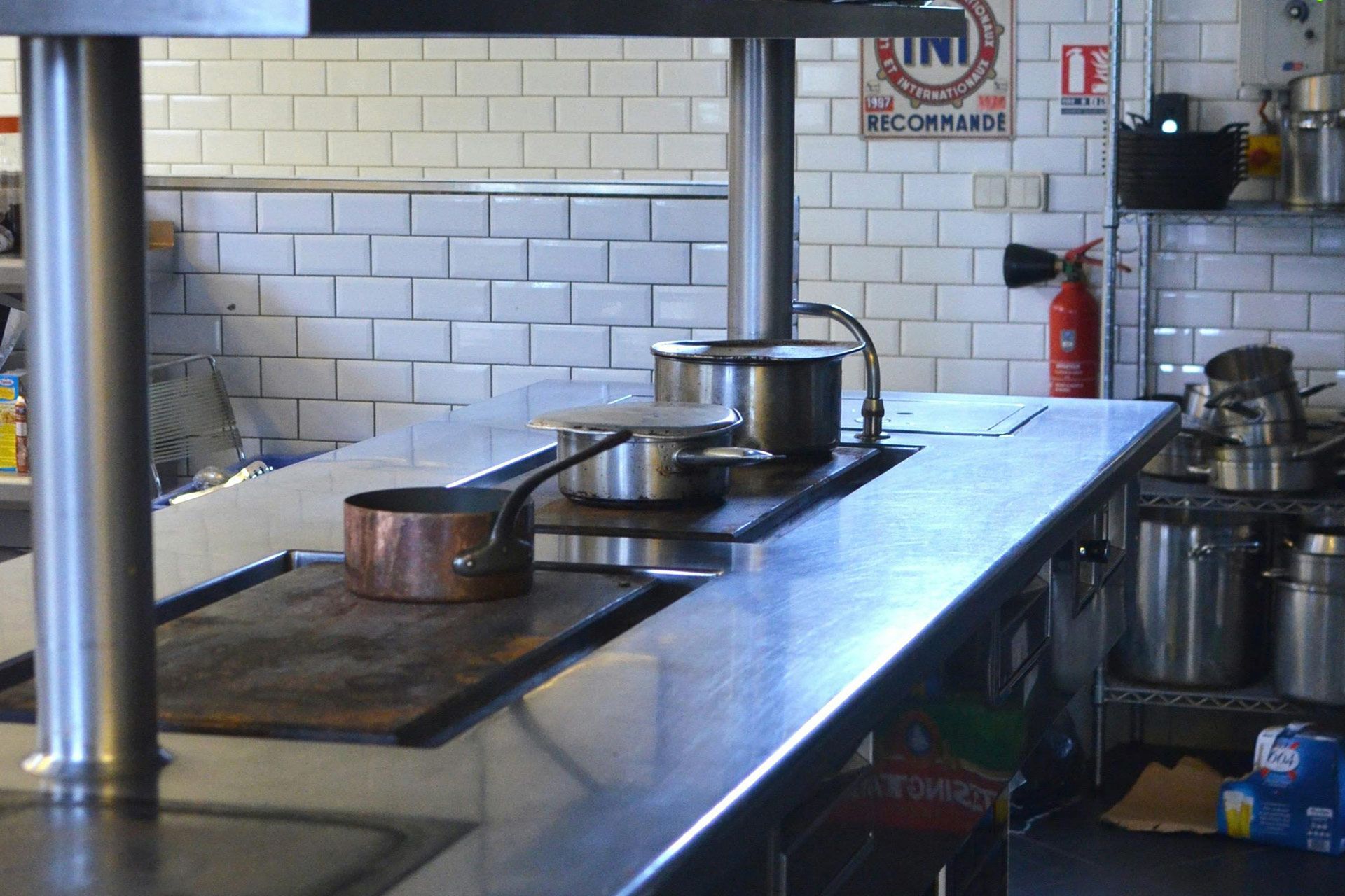 Commercial kitchen countertop with pots and stove, near tiled wall.