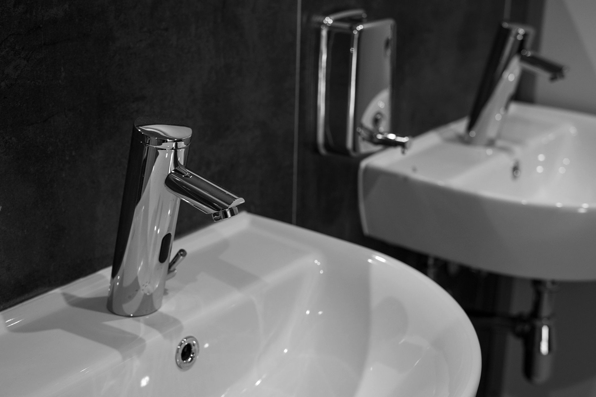 Two white sinks with chrome faucets in a bathroom, with a soap dispenser on the wall.