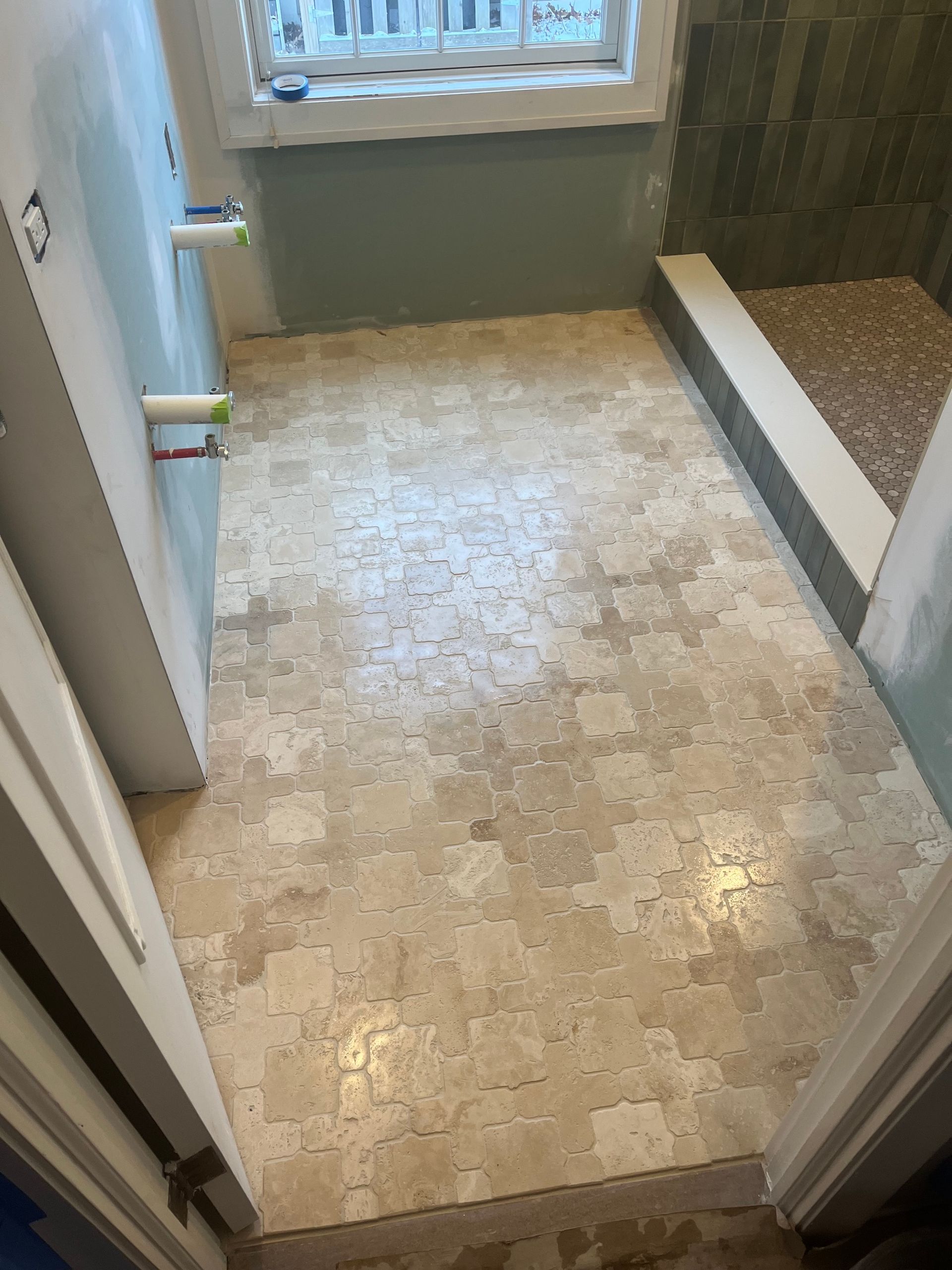 Bathroom with tiled floor and shower, light-colored tiles, green shower wall, and blue-gray wall above.