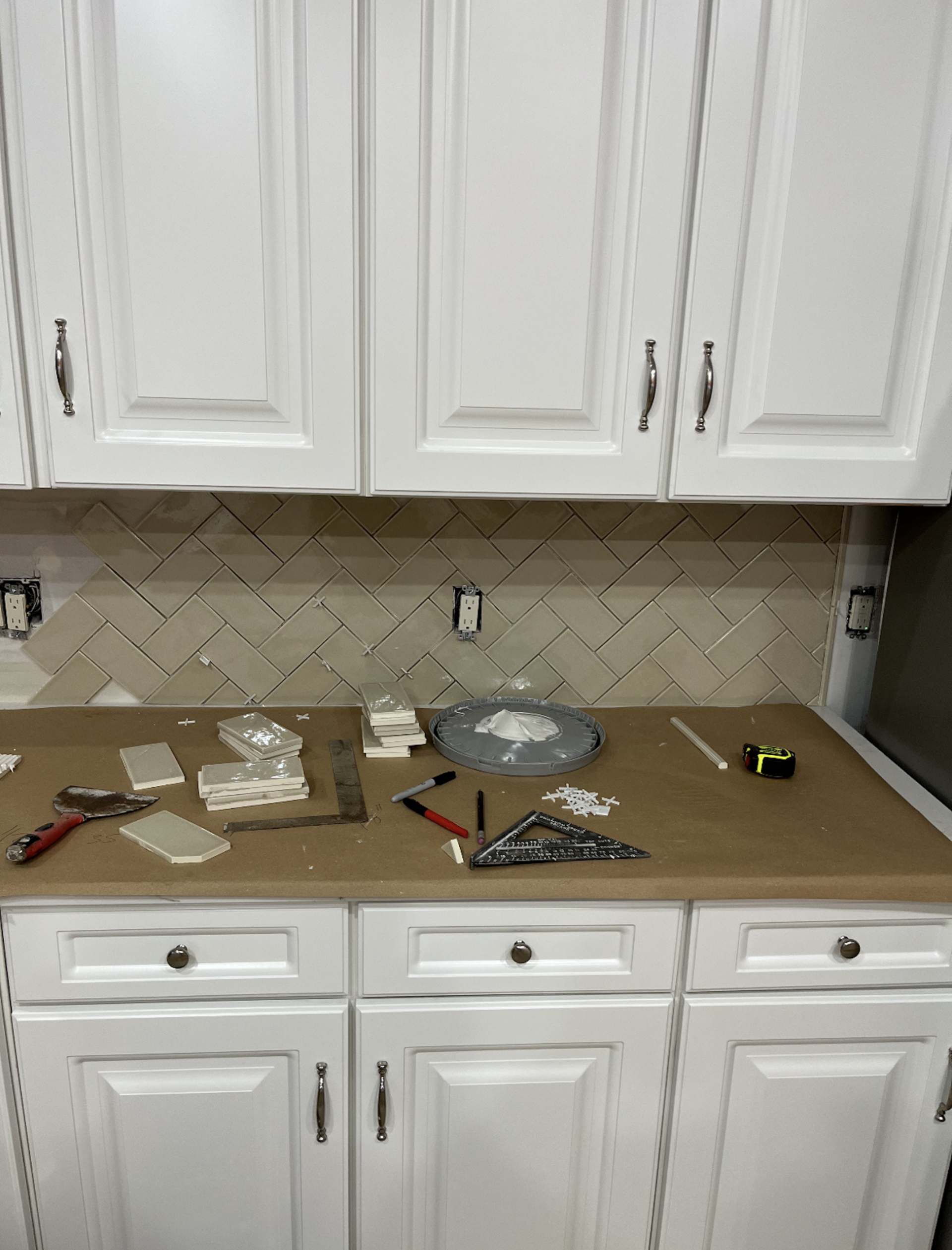Kitchen with white cabinets and a partially tiled backsplash in progress, tools on countertop.