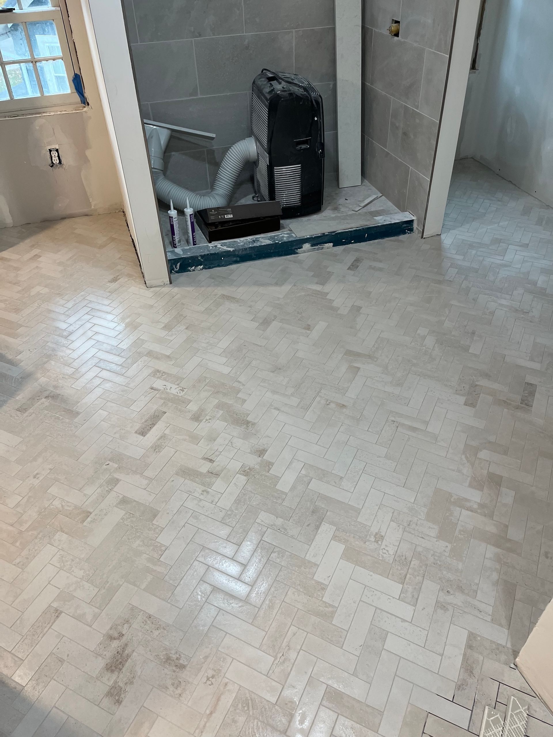 Herringbone pattern tile floor in a bathroom, adjacent to a tiled shower area under construction.
