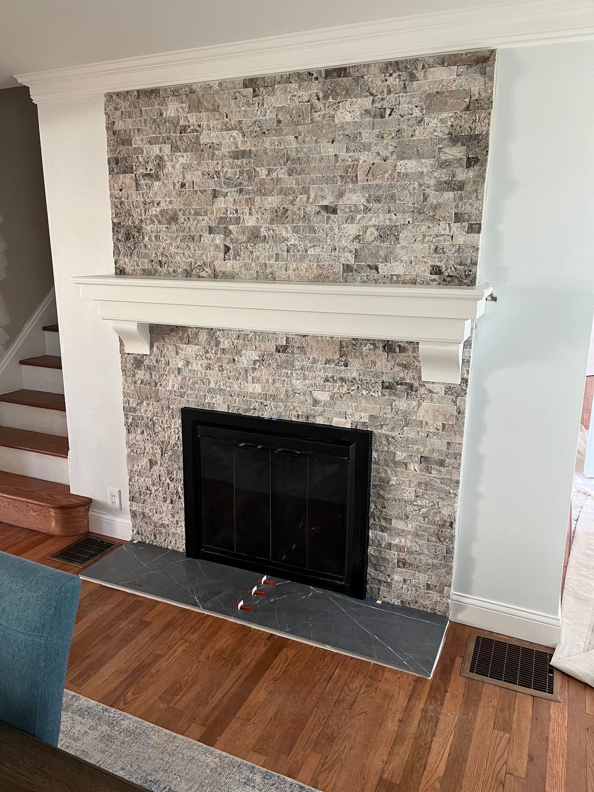 Fireplace with gray and white tile, black firebox, white mantel, and hardwood flooring.
