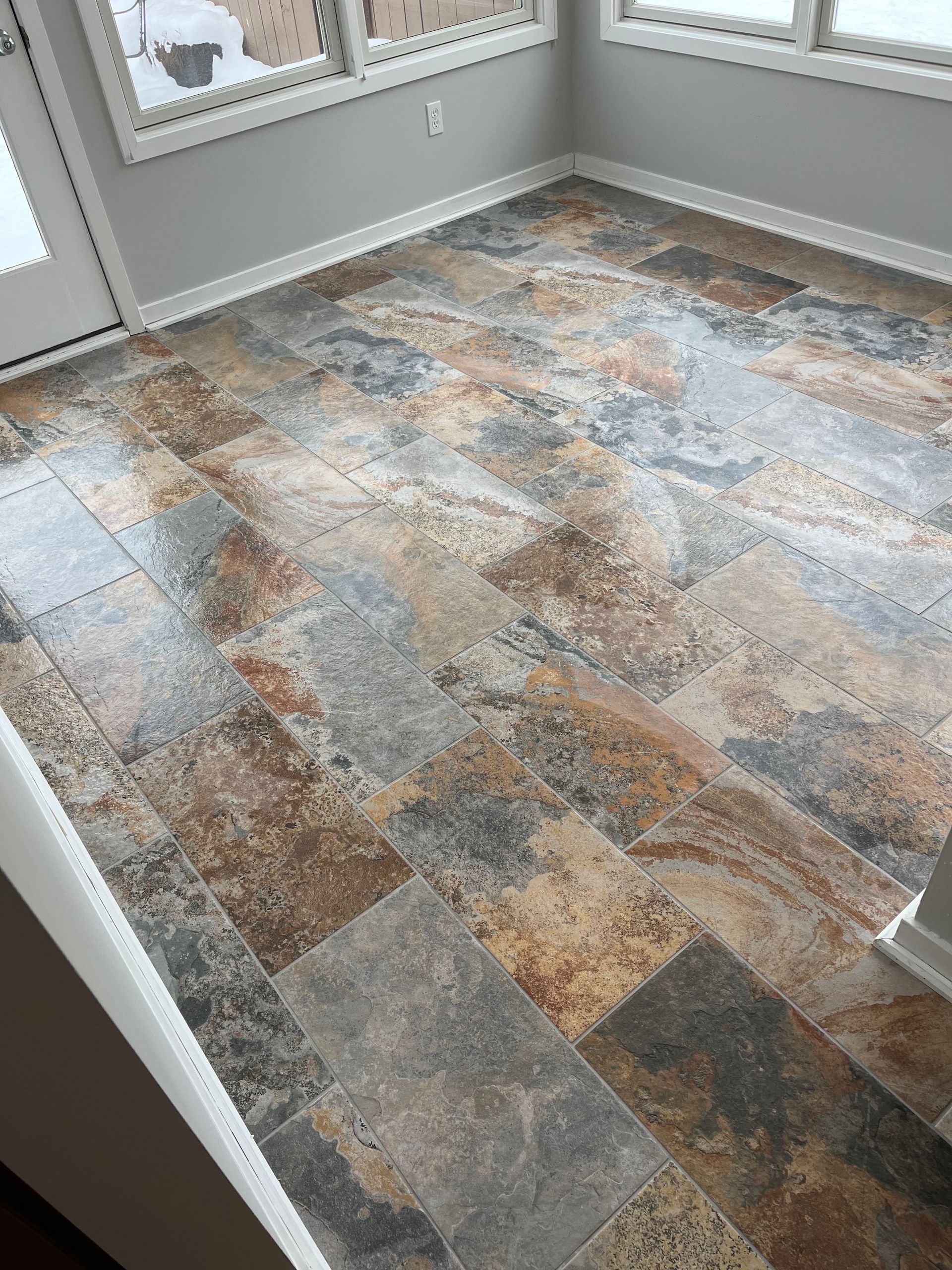 Sunroom with multi-colored stone-look flooring, white trim, and gray walls.