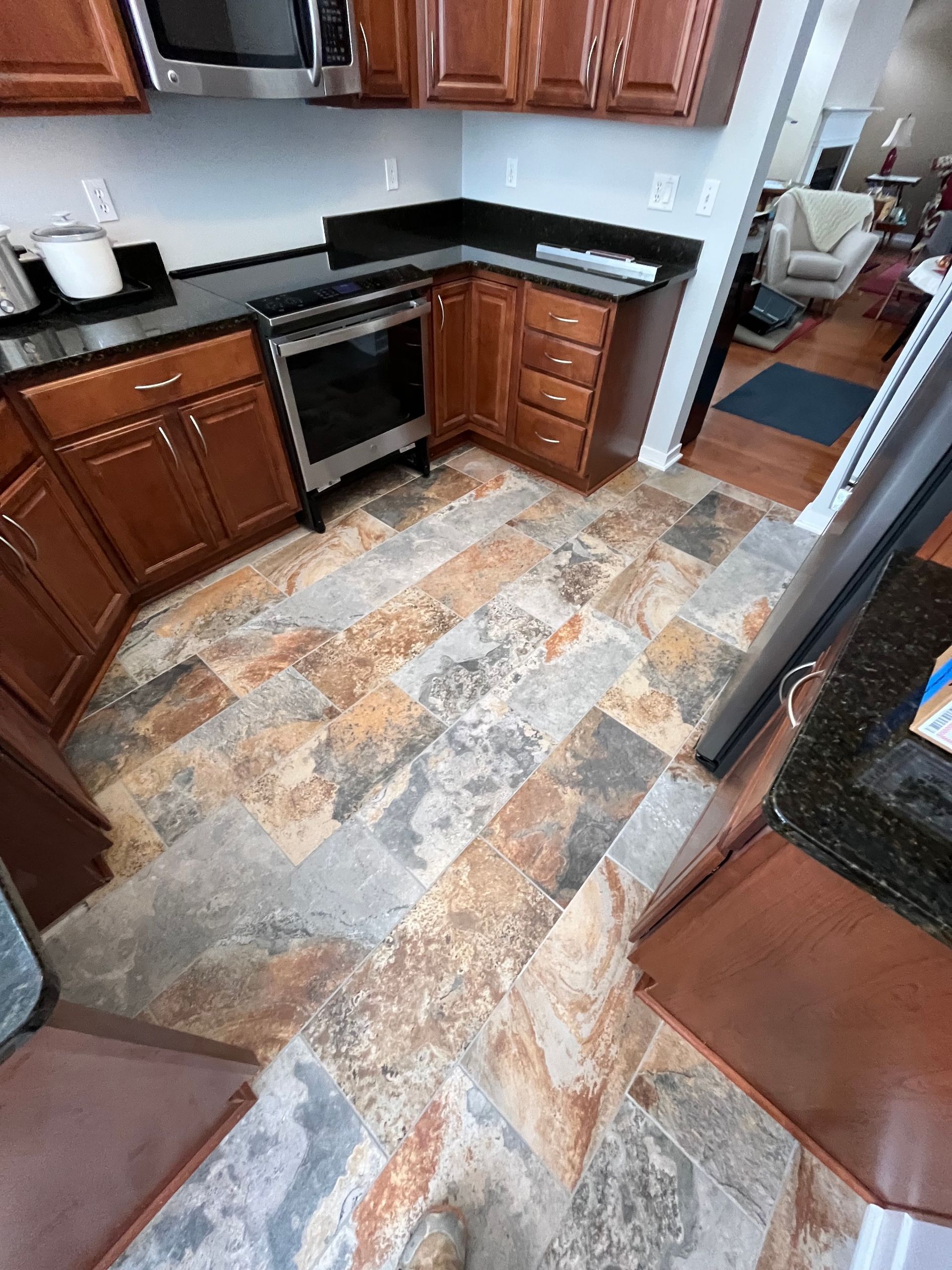Kitchen with brown cabinets, black countertops, and patterned tile flooring. A stainless steel oven is present.