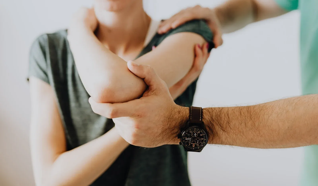 Person's arm being examined by another person's hands; indoors, pale skin, dark wristwatch.