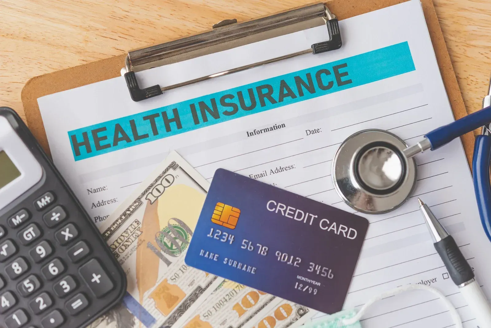 Health insurance form, credit card, stethoscope, calculator, cash, and pen on a clipboard.