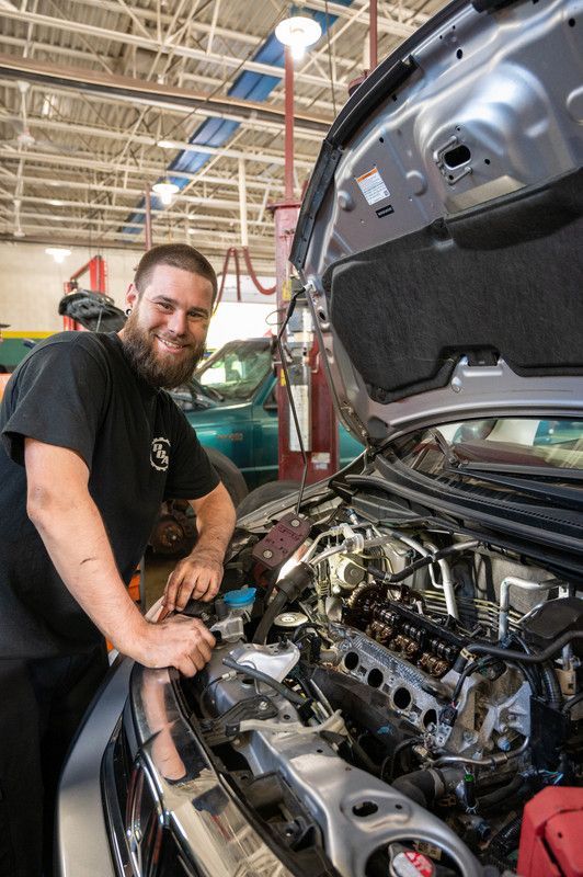 Mechanic smiling, working on a car engine in a brightly lit shop.