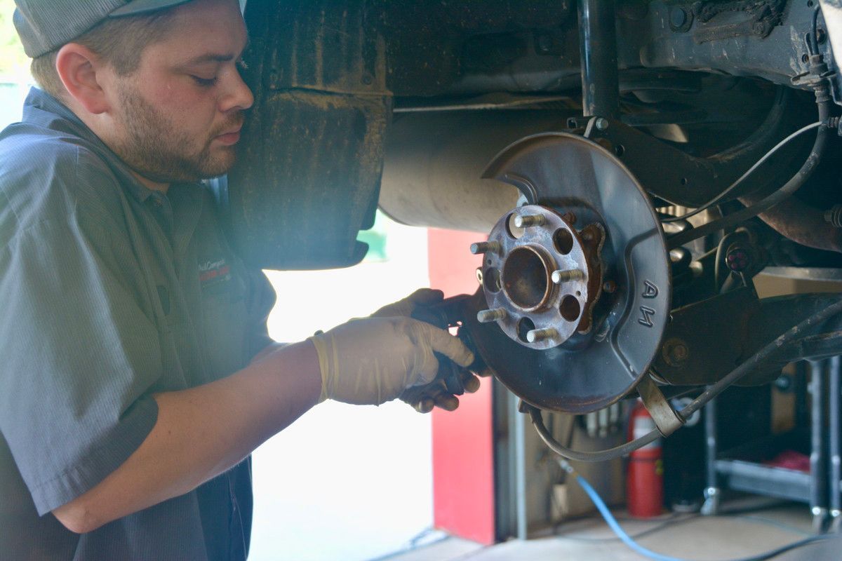 Mechanic in gloves working on a car's brake rotor, likely in a garage.
