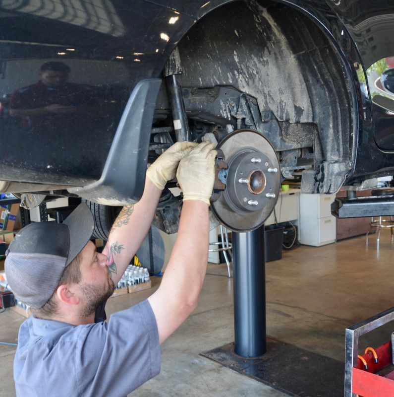 Mechanic working on a car's brakes, wearing gloves, in a garage.