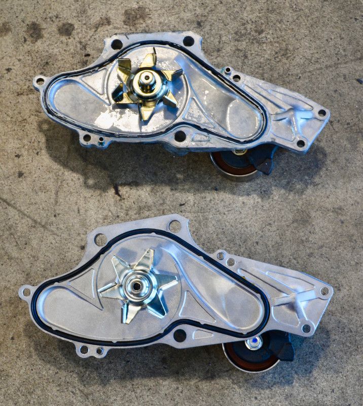 Two silver water pumps with black rubber seals and pulley wheels, side-by-side on a gray concrete surface.