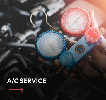 Person using gauges to service a car's AC system, red and blue gauges visible, engine bay in the background.