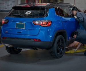 Two mechanics working on a blue SUV in a garage.